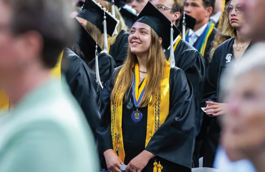 Graduate smiling and looking ahead in cap and gown with cords and medal.