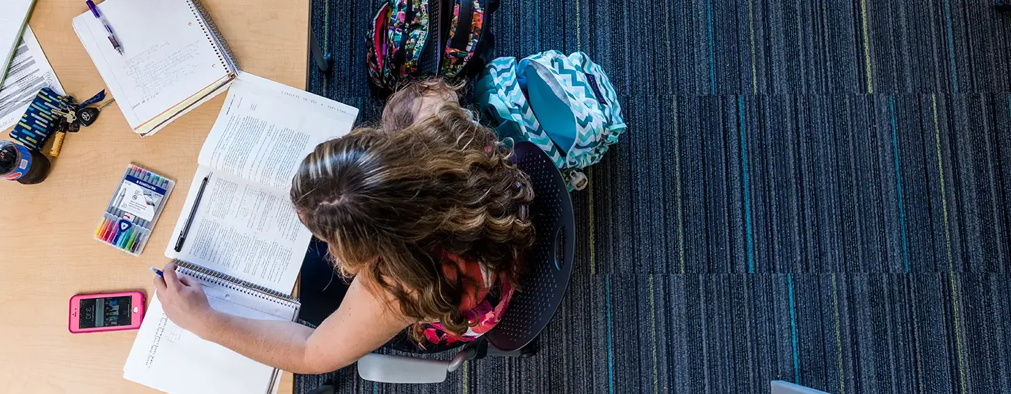 Two students sitting at a table, taking notes and reading textbooks.