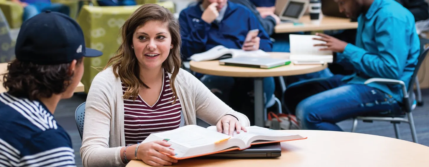 Woman discussing book with classmate.